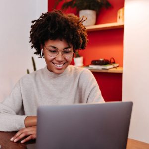 Woman in wireless headphones communicates via video link in laptop and posing in office with smile